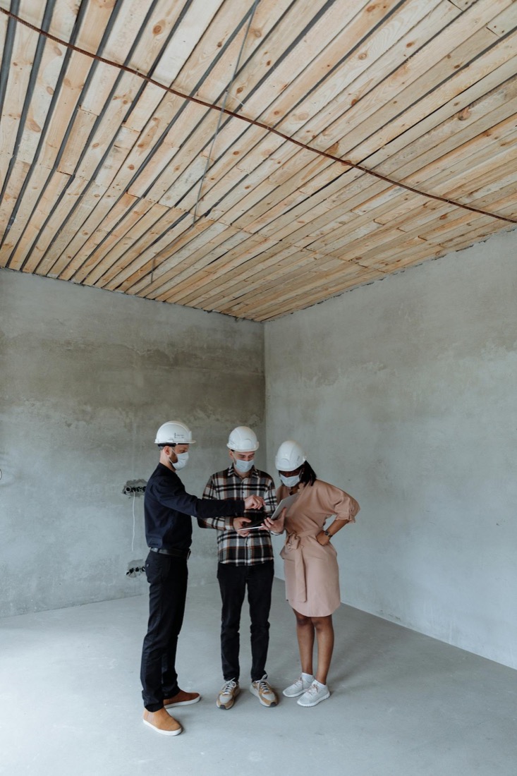 Team mit Schutzhelmen bespricht Unterlagen auf einer Baustelle.