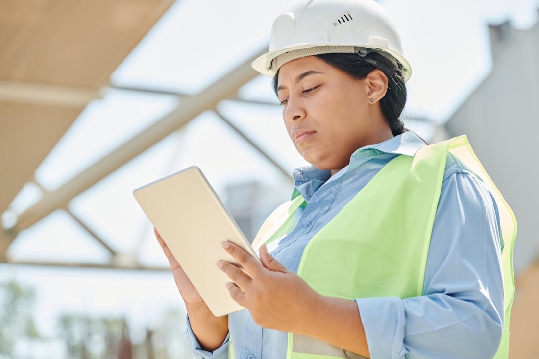 Person mit Schutzhelm und Tablet prüft technische Informationen vor Ort.